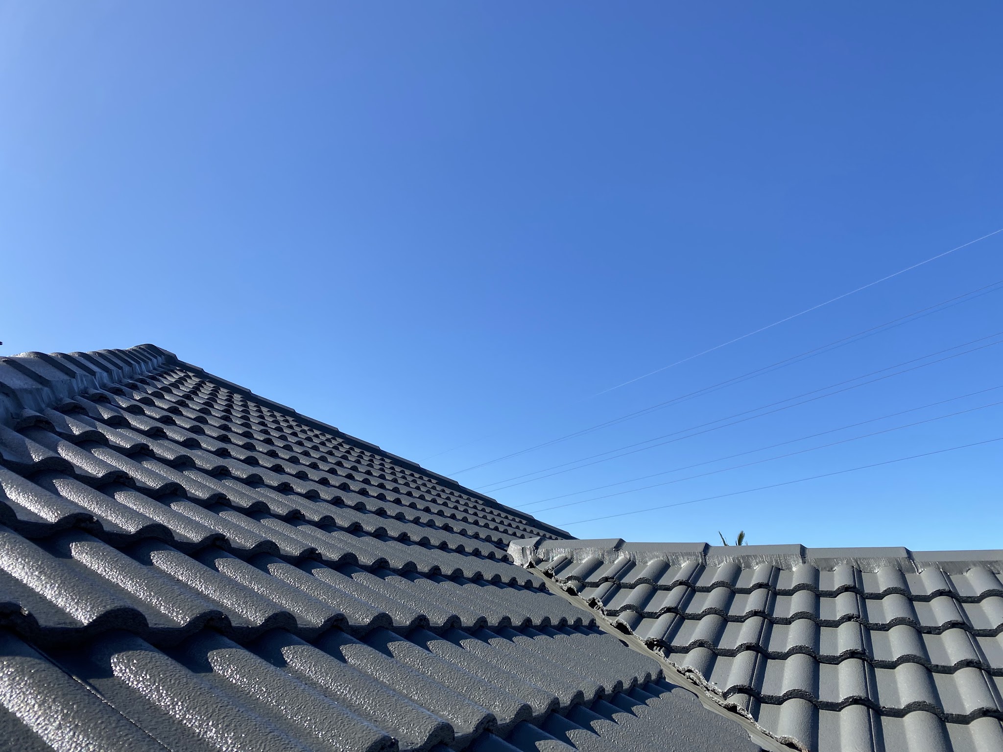 Freshly coated grey concrete tile roof ridge against a clear blue sky