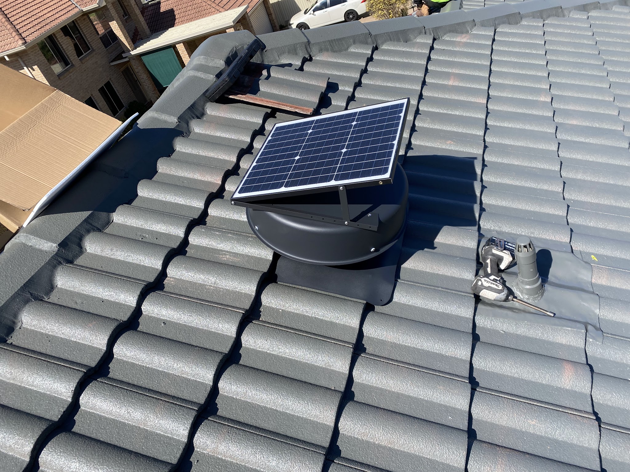 Solar roof ventilator being fitted into a grey tile roof, drill and tools resting on the tiles