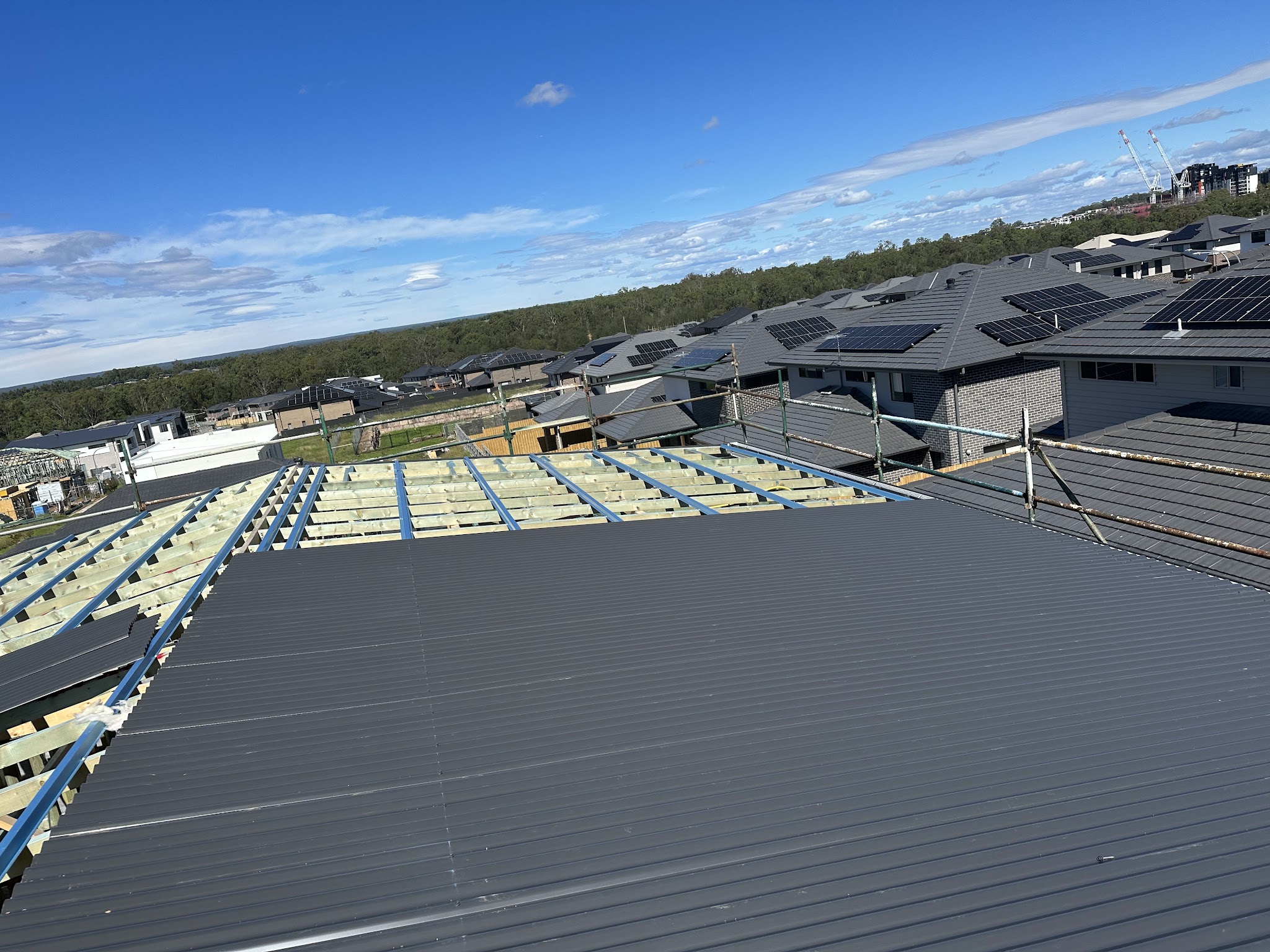 Metal roof going on over exposed battens on a new housing estate, cranes in the distance