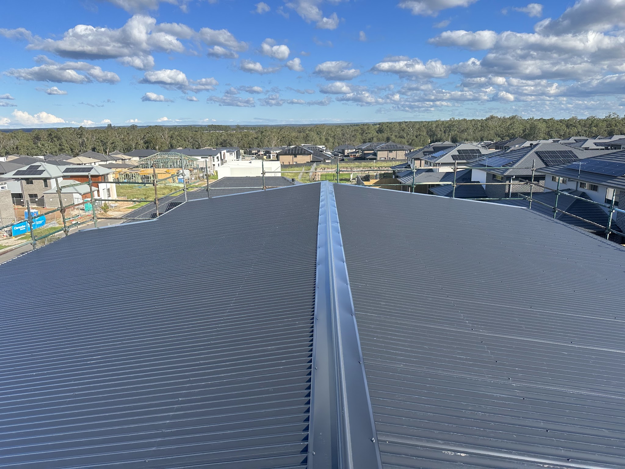Finished metal roof with a clean ridge line on a new home, blue sky and clouds above