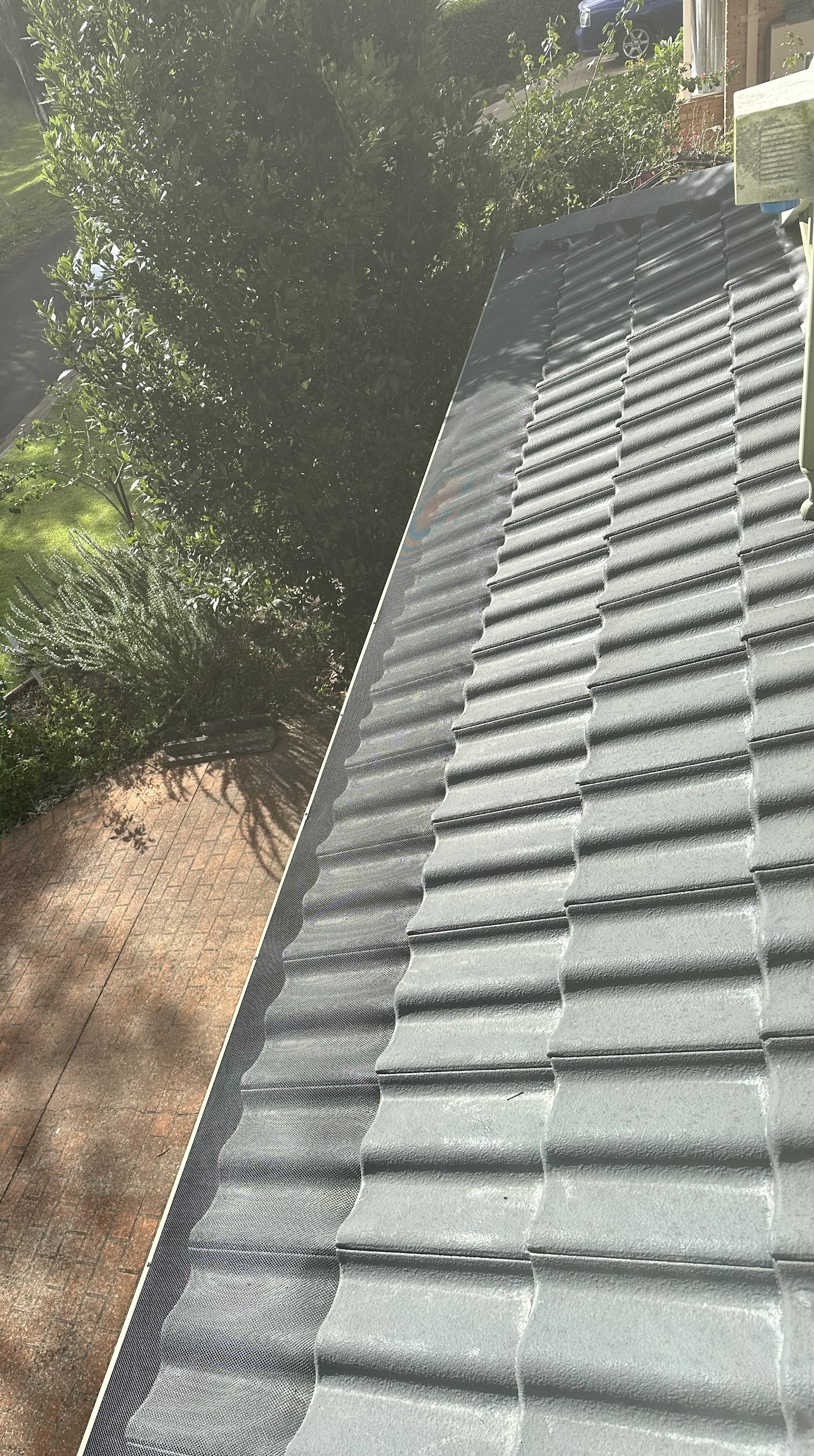 Looking down a freshly coated tile roof onto a paved driveway and garden
